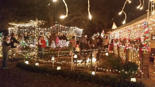 A festive outdoor scene at night, filled with colorful holiday lights and decorations, with people enjoying the display.