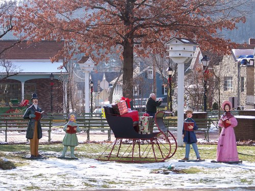 A festive scene with a decorated sleigh and life-sized figures singing carols in a snowy park.