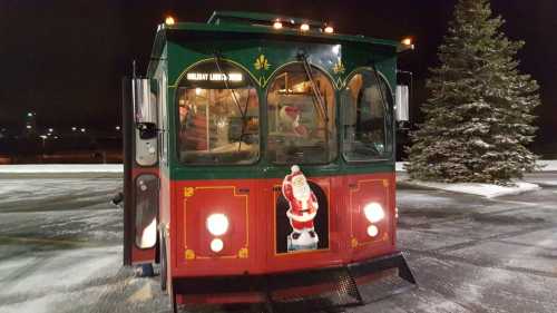 A festive green and red trolley with a Santa decoration, parked in a snowy area at night.