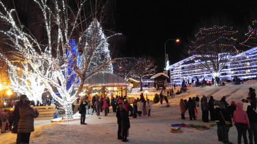 A festive winter scene with people enjoying lights and decorations in a snowy park at night.
