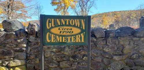 Sign for Gunntown Cemetery, established in 1790, surrounded by a stone wall and autumn foliage.