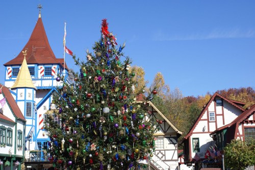 A decorated Christmas tree stands in front of colorful, festive buildings under a clear blue sky.