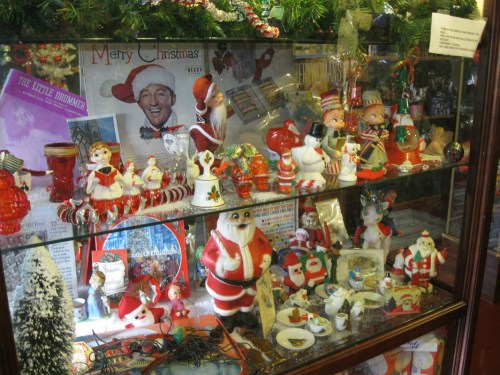 A festive display case filled with vintage Christmas decorations, including Santa figurines and holiday-themed items.