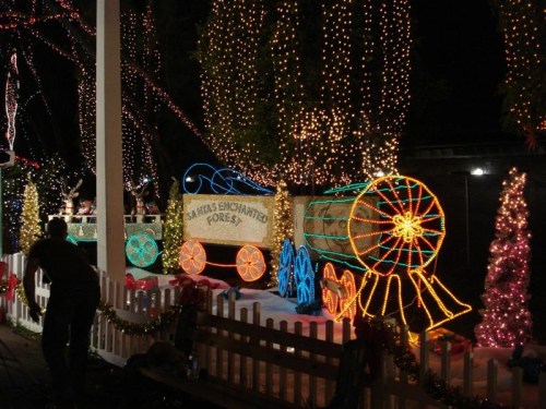 Colorful holiday lights decorate a train and trees in a festive outdoor display.