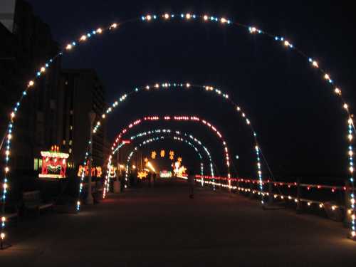 A brightly lit walkway at night, adorned with colorful arches of lights and festive decorations along the sides.