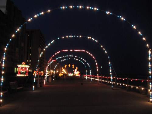 A brightly lit walkway at night, adorned with colorful arches of lights and festive decorations along the sides.