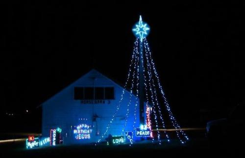 A house decorated with blue Christmas lights, featuring a star on top and signs that say "Happy Birthday Jesus" and "Peace."
