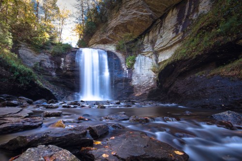 A serene waterfall cascades over rocky cliffs, surrounded by lush greenery and autumn foliage.