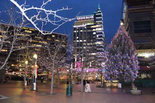 A festive plaza at night, featuring a large decorated Christmas tree and buildings adorned with colorful lights.