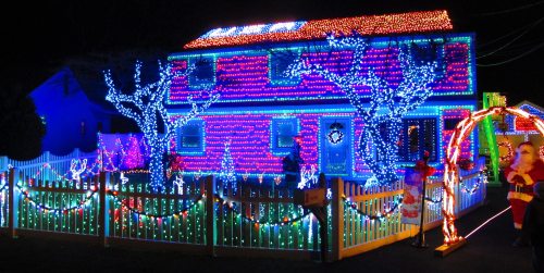 A brightly lit house decorated with colorful Christmas lights, featuring illuminated trees and festive decorations.