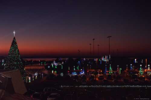 A vibrant sunset over a festive display of Christmas lights and decorations, including a large tree and various illuminated shapes.