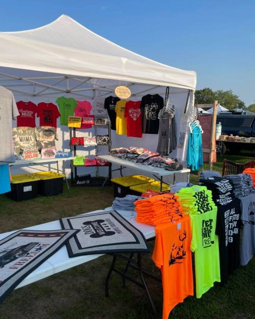 A vibrant outdoor market stall displaying a variety of colorful t-shirts and merchandise under a white canopy.