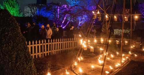 A nighttime scene with people walking along a path lit by lanterns, surrounded by colorful lights and trees.