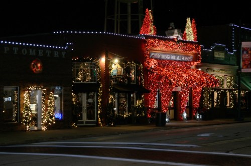 A festive storefront decorated with colorful Christmas lights and holiday decorations at night.