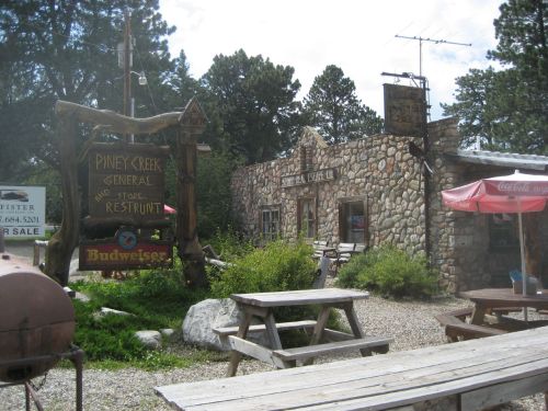 A rustic stone building with a sign for Pine Creek General Store and Restaurant, surrounded by trees and picnic tables.