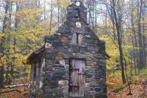 A small, weathered stone building surrounded by autumn trees with colorful leaves.