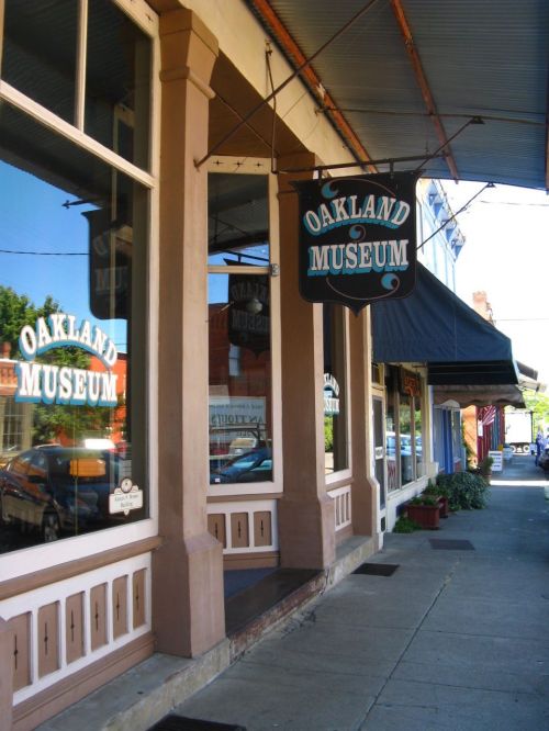Exterior view of the Oakland Museum, featuring a sign and storefront along a sidewalk.