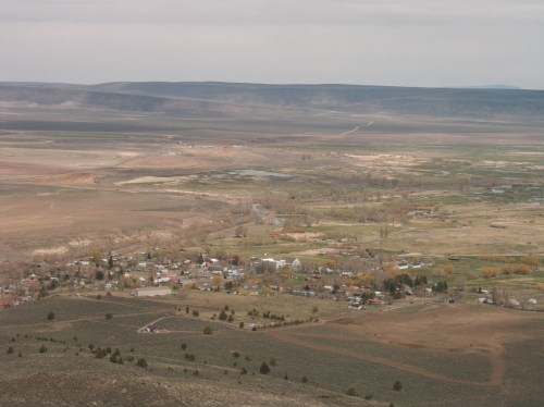 A panoramic view of a small town surrounded by vast, open landscapes and distant mountains under a cloudy sky.