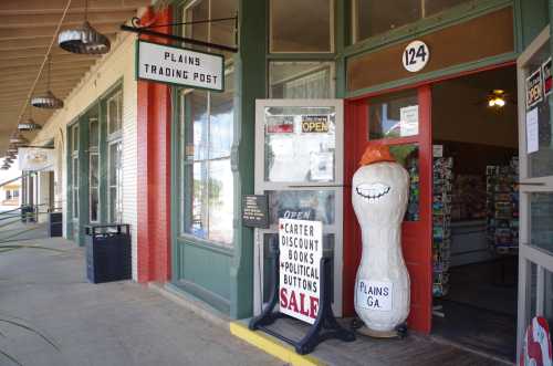 Exterior of Plains Trading Post with a large peanut statue and signs advertising open hours and sales.