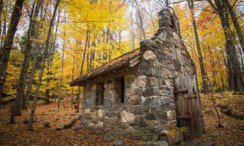 A rustic stone cabin surrounded by vibrant autumn foliage in a serene forest setting.