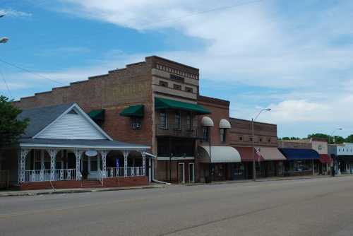 A quiet street scene featuring historic brick buildings and storefronts under a blue sky with scattered clouds.