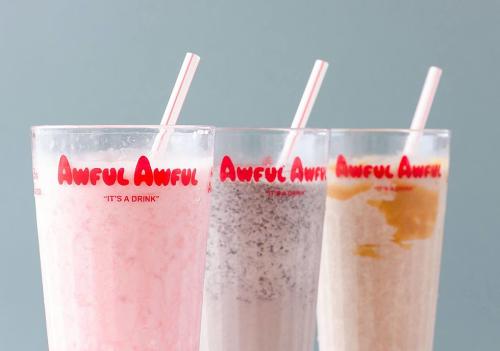Three tall glasses of colorful milkshakes with straws, labeled "Awful Awful," against a light blue background.