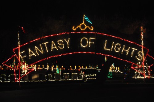 A brightly lit sign reading "Fantasy of Lights" surrounded by colorful holiday decorations at night.