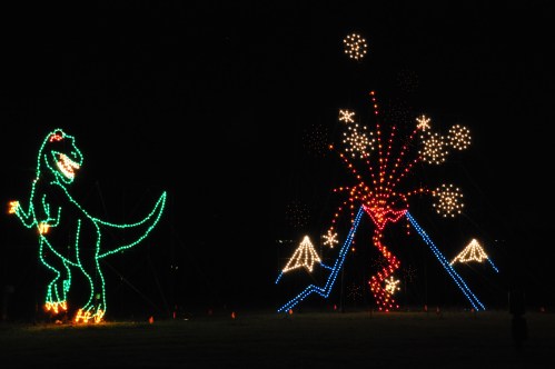 A colorful light display featuring a dinosaur and a volcano with fireworks against a dark night sky.