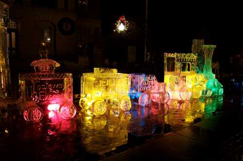 Colorful ice sculptures of a train, illuminated with vibrant lights, displayed on a wet surface at night.