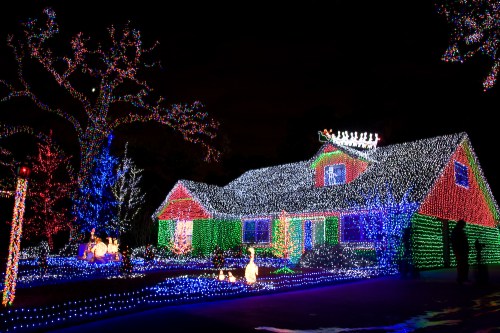 A brightly lit house decorated with colorful Christmas lights, surrounded by illuminated trees and festive decorations.
