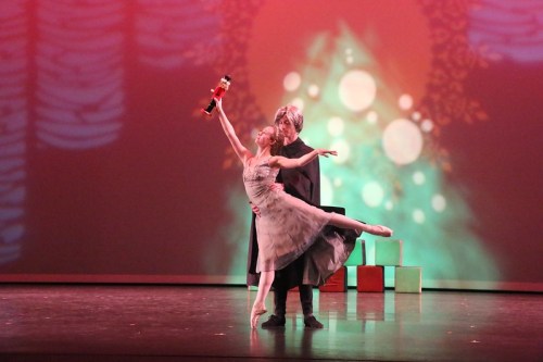 A ballet performance featuring a dancer in a gray dress and a partner, set against a colorful, festive backdrop.