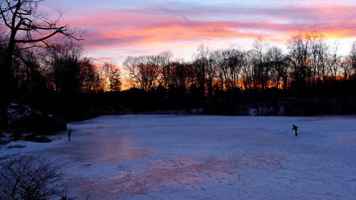 A serene winter scene with a frozen lake at sunset, featuring silhouettes of skaters against a colorful sky.