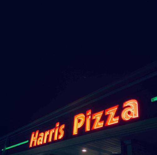Neon sign of "Harris Pizza" illuminated at night against a dark sky.