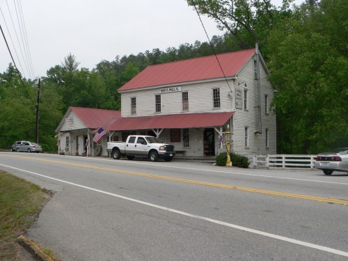 A historic building with a red roof, featuring a porch and American flag, located along a rural road.
