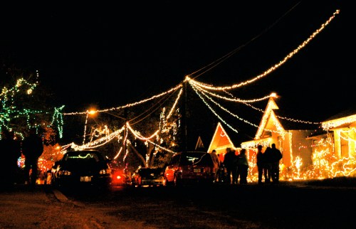 A festive street at night, adorned with colorful holiday lights and decorations, with people enjoying the scene.