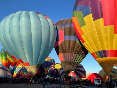 Colorful hot air balloons fill the sky at a festival, with people gathered below in a vibrant, festive atmosphere.