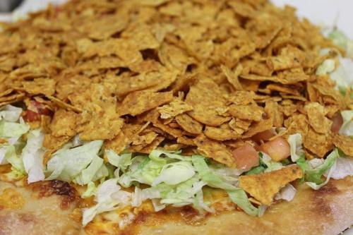 A pizza topped with shredded lettuce, diced tomatoes, and a generous layer of crushed tortilla chips.