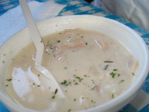 A bowl of creamy soup with chunks of meat and herbs, served with a plastic spoon.