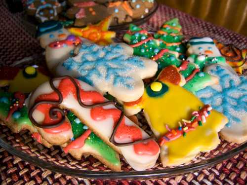 A colorful assortment of decorated holiday cookies, including trees, snowmen, and candy canes, on a plate.