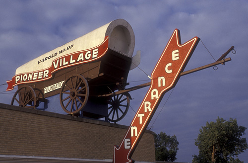 A large, vintage wagon atop a building, with a sign reading "Pioneer Village" and an arrow pointing to "Entertainment."