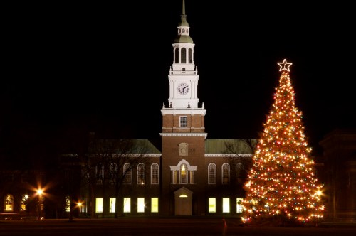 A brightly lit Christmas tree stands in front of a historic building with a clock tower, illuminated at night.