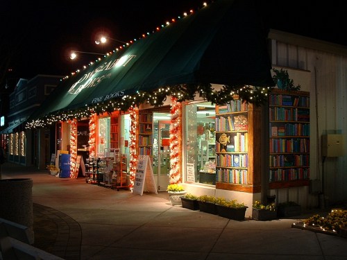 A cozy bookstore at night, adorned with festive lights and decorations, inviting customers inside.