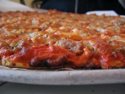Close-up of a freshly baked pizza with a golden crust, melted cheese, and toppings, resting on a round plate.