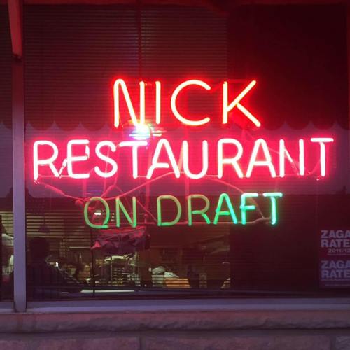 Neon sign in a restaurant window reads "NICK RESTAURANT ON DRAFT" with reflections and warm lighting.