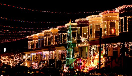 Colorful holiday lights adorn houses and a Christmas tree, creating a festive atmosphere at night.