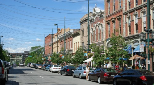 A charming street lined with historic brick buildings, trees, and parked cars under a clear blue sky.