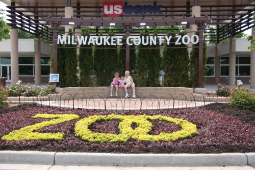 A family sits at the entrance of the Milwaukee County Zoo, surrounded by colorful flower arrangements.