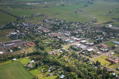 Aerial view of a small town surrounded by green fields and farmland, featuring residential and commercial buildings.