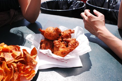 A basket of fried chicken pieces sits on a table next to a plate of crispy potato chips.