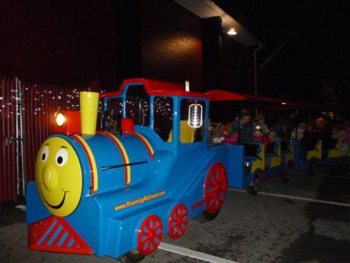 A colorful children's train ride at night, with kids seated in a brightly painted train car.